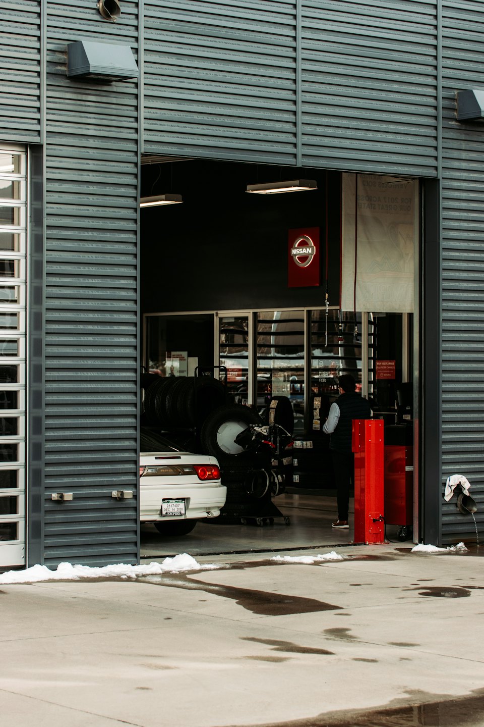 Service technician works on a white car in a garage bay.