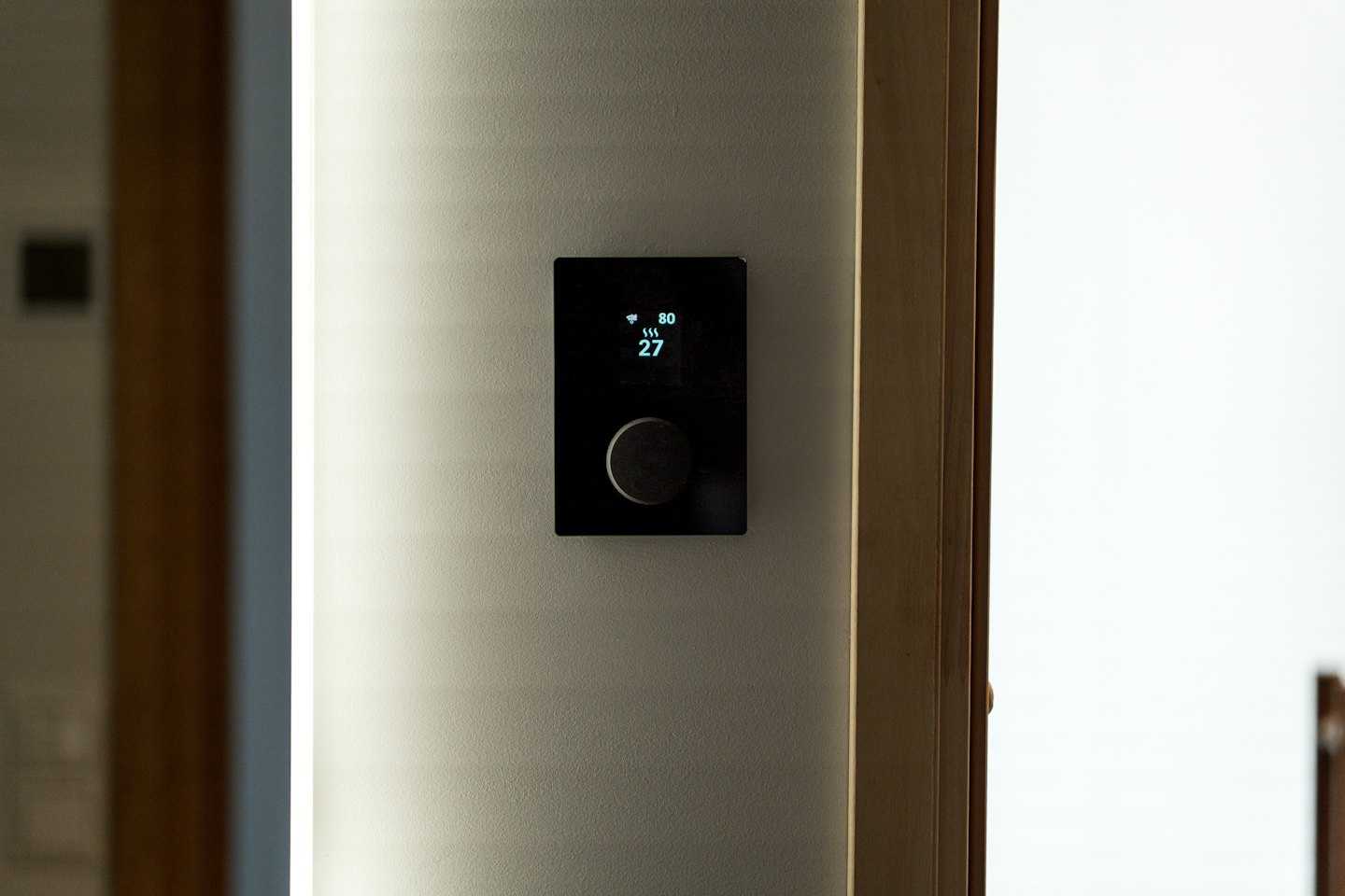 Modern smart thermostat displaying room temperature on wall.