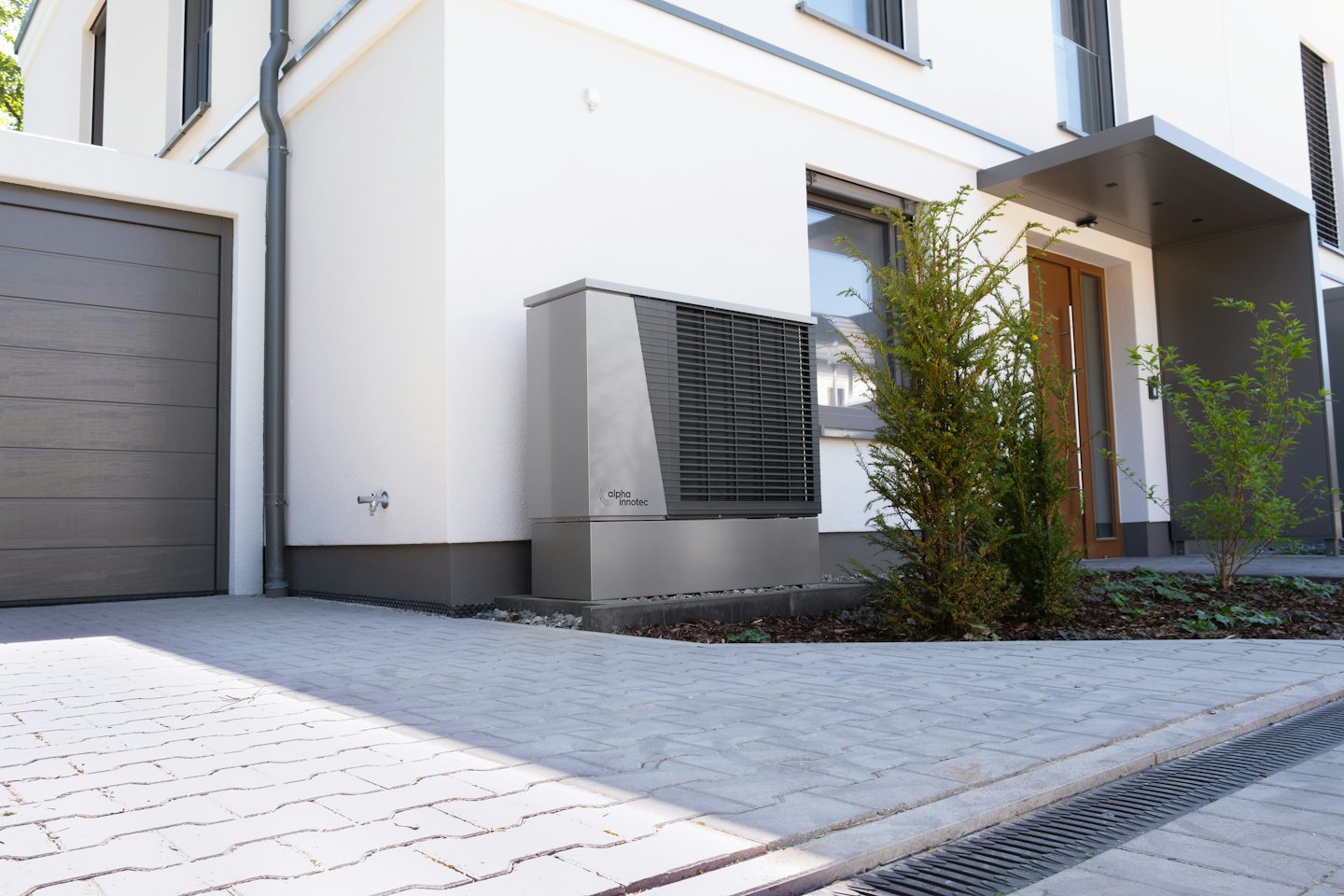 Heat pump mounted on a stucco wall next to a garage door.